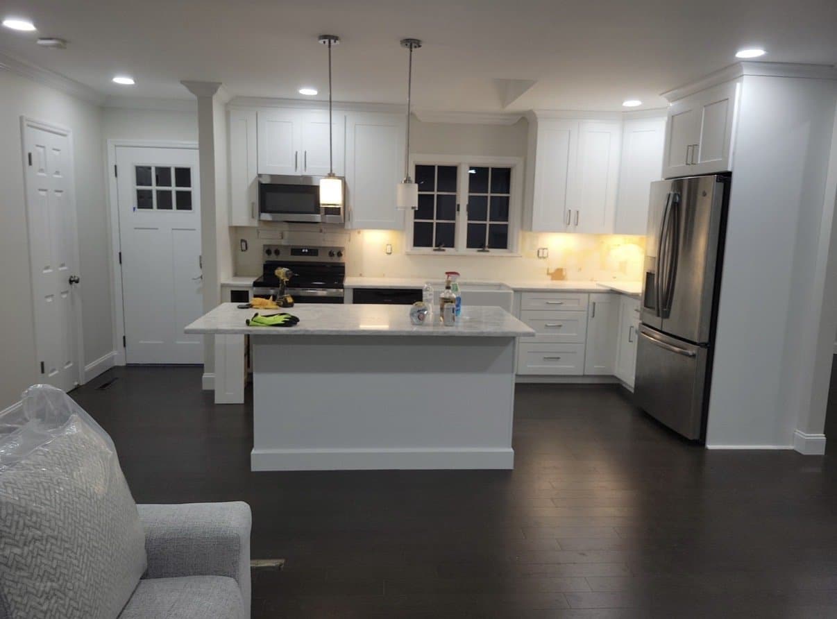 After: The finished kitchen: white shaker cabinets, a marble-look island, two pendants and dark hardwood.