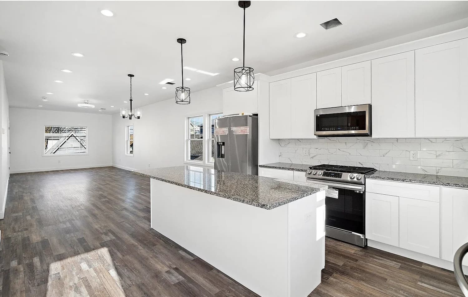 A finished kitchen in an empty house: white shaker cabinets, a granite island, black pendants.