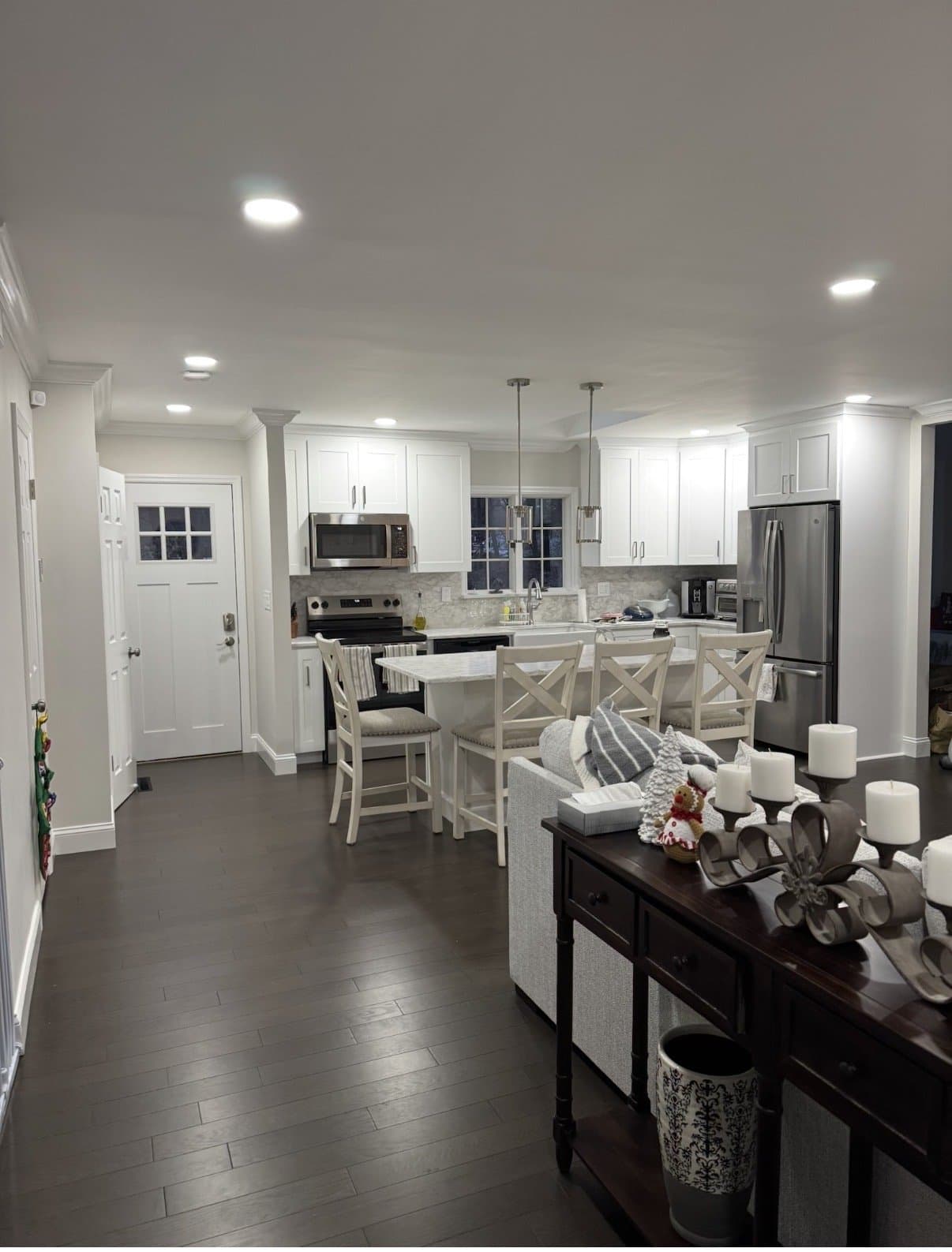 The finished kitchen in the evening, with island seating, pendants and a marble-look backsplash.