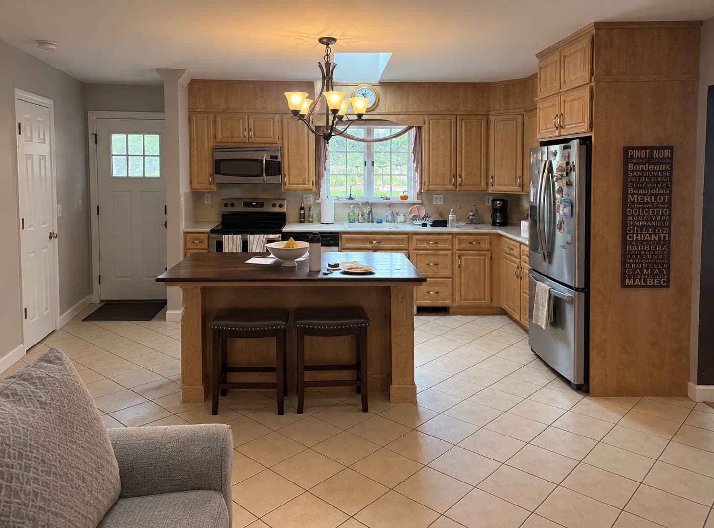 Before: The original maple kitchen with a dark wood-top island, a chandelier and tile flooring.
